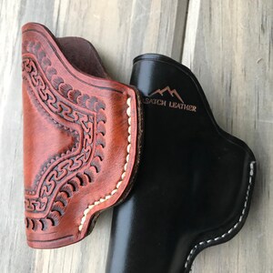 Peut inclure: Deux &eacute;tuis en cuir, l'un brun avec des coutures complexes et l'autre noir, tous deux avec des coutures blanches. L'&eacute;tui noir porte le texte "SATCH LEATHER" en relief.