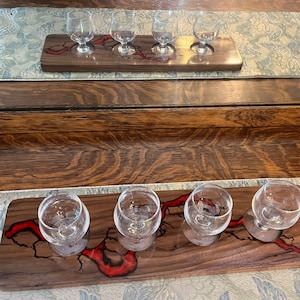 May include: A wooden serving tray with five glass holders for tasting different beverages. The tray has a red epoxy resin inlay that resembles a river or stream.