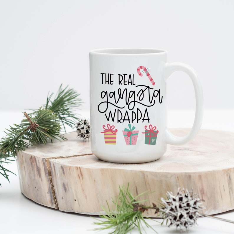 Pu&ograve; includere: Tazza in ceramica bianca con un design in bianco e nero che dice "The Real Gangsta Wrappa". Il design include anche una canna di zucchero e tre regali avvolti.