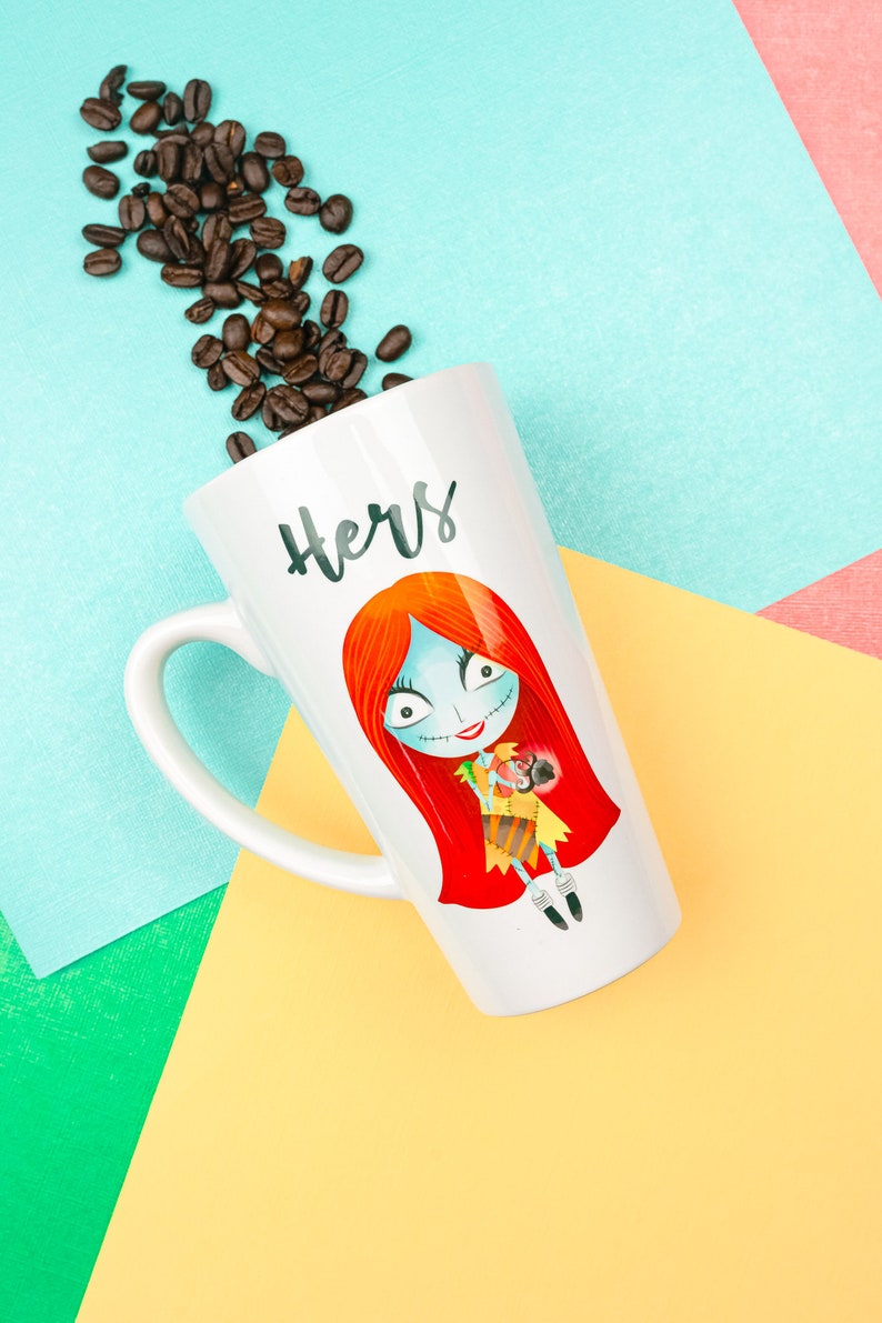 Może przedstawiać: Biały kubek ceramiczny z postacią z kresk&oacute;wki w kolorze czerwonym, białym i czarnym, trzymającą małą, brązową postać. Kubek ma napis "Hers" w czarnych literach. Ziarna kawy są rozrzucone wok&oacute;ł kubka na niebieskim, zielonym i ż&oacute;łtym tle.