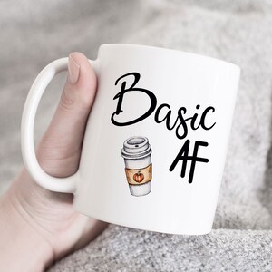 May include: White ceramic mug with a black design that says "Basic AF" and a drawing of a coffee cup with a pumpkin on it.