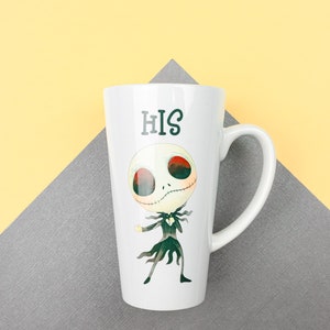 Może przedstawiać: Biały kubek ceramiczny z czarno-zieloną postacią z kresk&oacute;wki i nadrukiem słowa "HIS" z przodu.