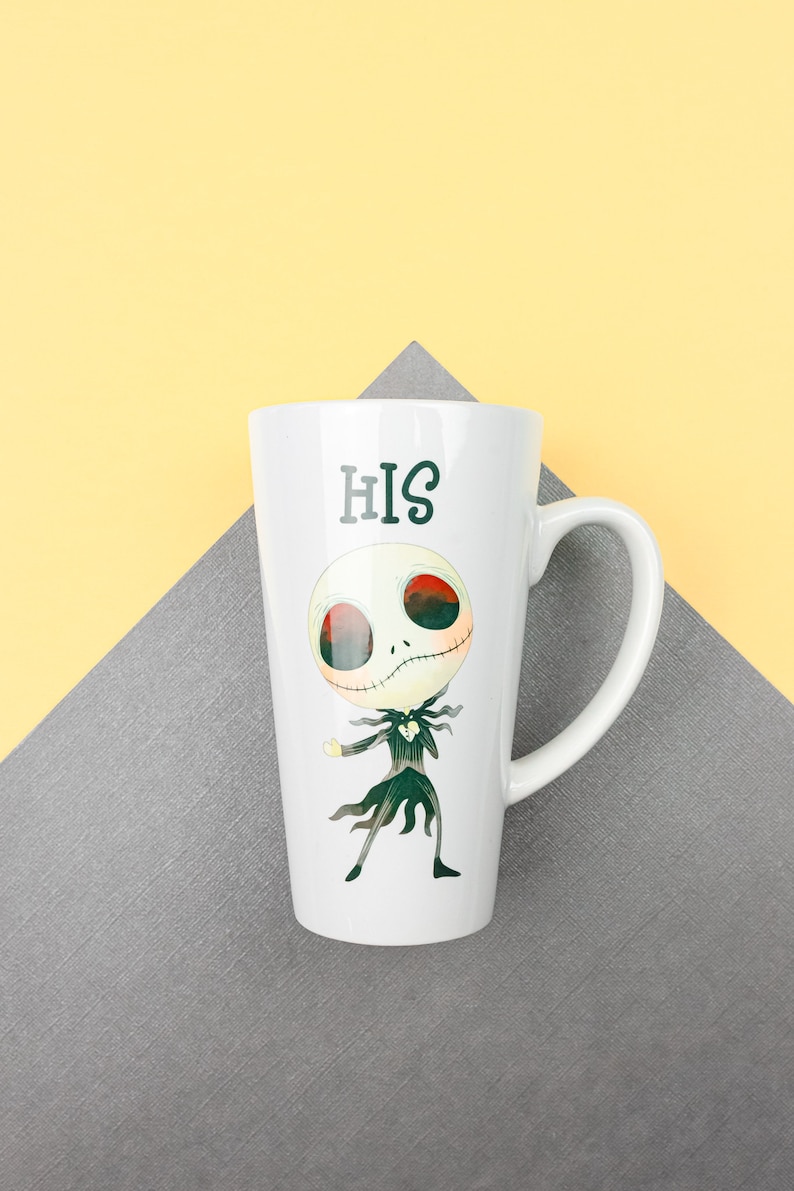 Może przedstawiać: Biały kubek ceramiczny z czarno-zieloną postacią z kresk&oacute;wki i nadrukiem słowa "HIS" z przodu.