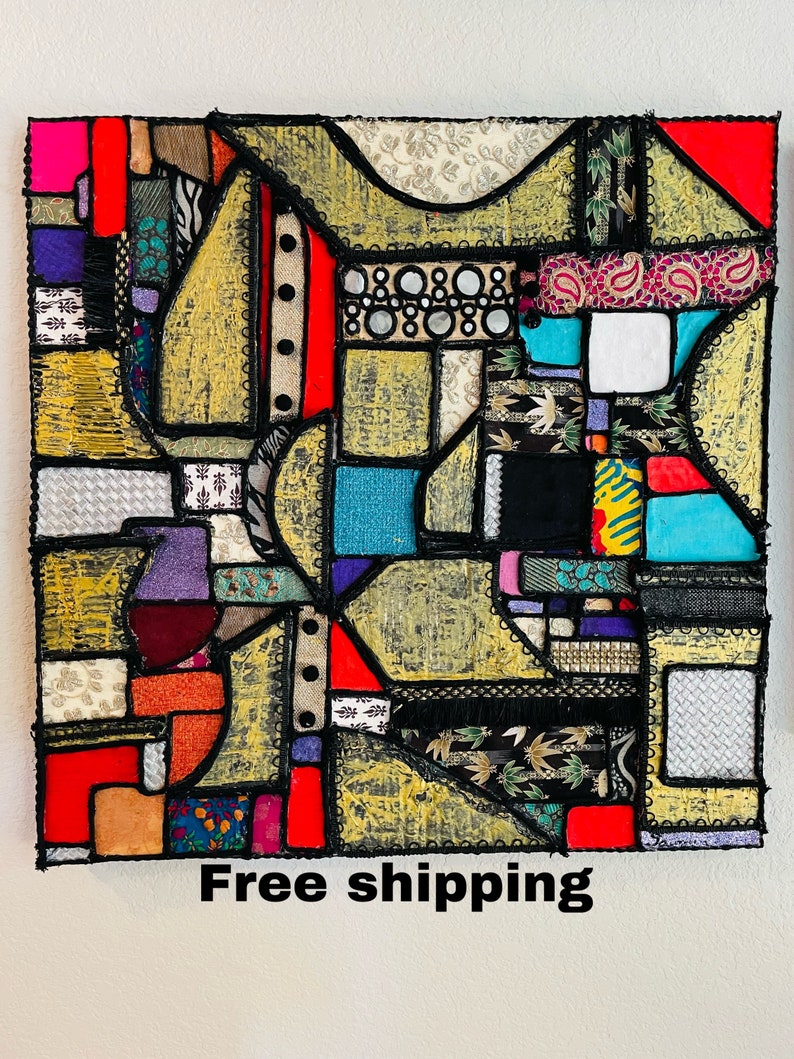 Op de afbeelding: Abstract kunstwerk gemaakt van kleurrijke stoffen die in een geometrisch patroon aan elkaar zijn genaaid. De stof is een mix van texturen en patronen, waaronder paisley, bloemen en geometrische prints. Het stuk is omlijst met zwart en heeft een gouden achtergrond.