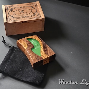 May include: A rectangular wooden lighter featuring a central wavy inlay of translucent green resin, accompanied by a small black drawstring pouch and a matching wooden storage box with an engraved decorative border and the initials WG.