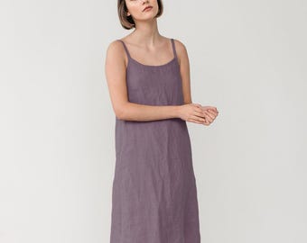 Puede incluir: Un vestido tipo lencero sin mangas hasta la rodilla en un color morado polvoriento apagado. La prenda presenta un escote redondo sencillo y tirantes finos, con una silueta de corte recto que cae holgadamente desde el corpiño hasta el dobladillo.