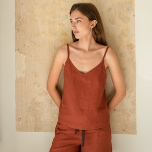 Könnte beinhalten: Ein Tanktop und passende Shorts aus Leinen in Rostfarbe. Das Oberteil hat einen V-Ausschnitt und dünne Träger. Die Shorts haben einen Kordelzugbund.