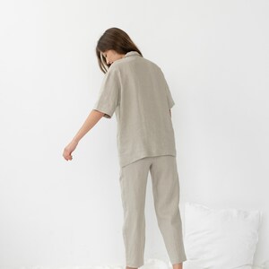 Pu&ograve; includere: Una persona indossa una camicia di lino beige chiaro e pantaloni abbinati. La camicia ha un colletto e maniche corte. I pantaloni sono corti e hanno una gamba dritta.