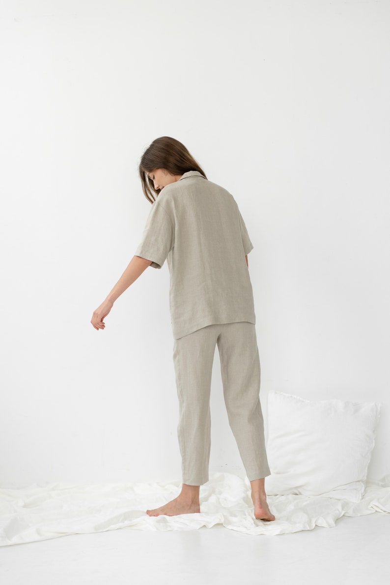 Pu&ograve; includere: Una persona indossa una camicia di lino beige chiaro e pantaloni abbinati. La camicia ha un colletto e maniche corte. I pantaloni sono corti e hanno una gamba dritta.