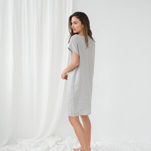 May include: A woman wearing a light gray linen dress with short sleeves. The dress is knee-length and has a relaxed fit.