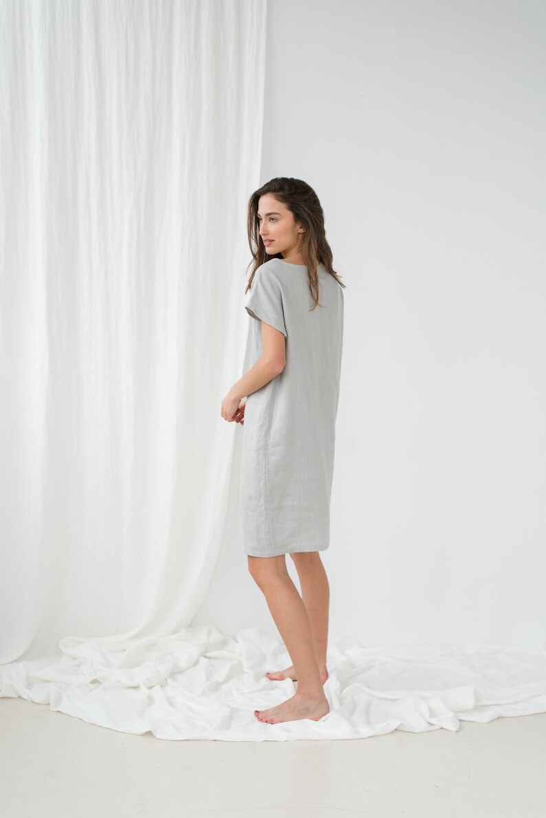 May include: A woman wearing a light gray linen dress with short sleeves. The dress is knee-length and has a relaxed fit.
