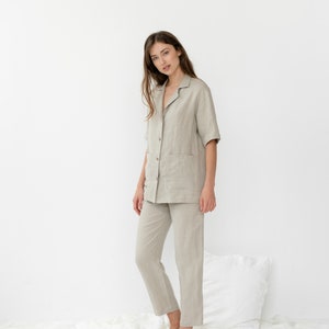 Pu&ograve; includere: Una persona indossa una camicia di lino beige chiaro e pantaloni abbinati. La camicia ha un colletto, maniche corte e una chiusura con bottoni sul davanti. I pantaloni hanno una gamba dritta e una vestibilit&agrave; rilassata.
