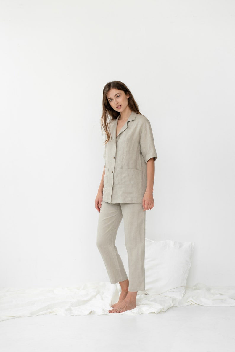 Pu&ograve; includere: Una persona indossa una camicia di lino beige chiaro e pantaloni abbinati. La camicia ha un colletto, maniche corte e una chiusura con bottoni sul davanti. I pantaloni hanno una gamba dritta e una vestibilit&agrave; rilassata.