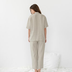 Pu&ograve; includere: Una persona indossa una camicia di lino beige chiaro e pantaloni abbinati. La camicia ha un colletto e maniche corte. I pantaloni sono corti e hanno una gamba dritta.