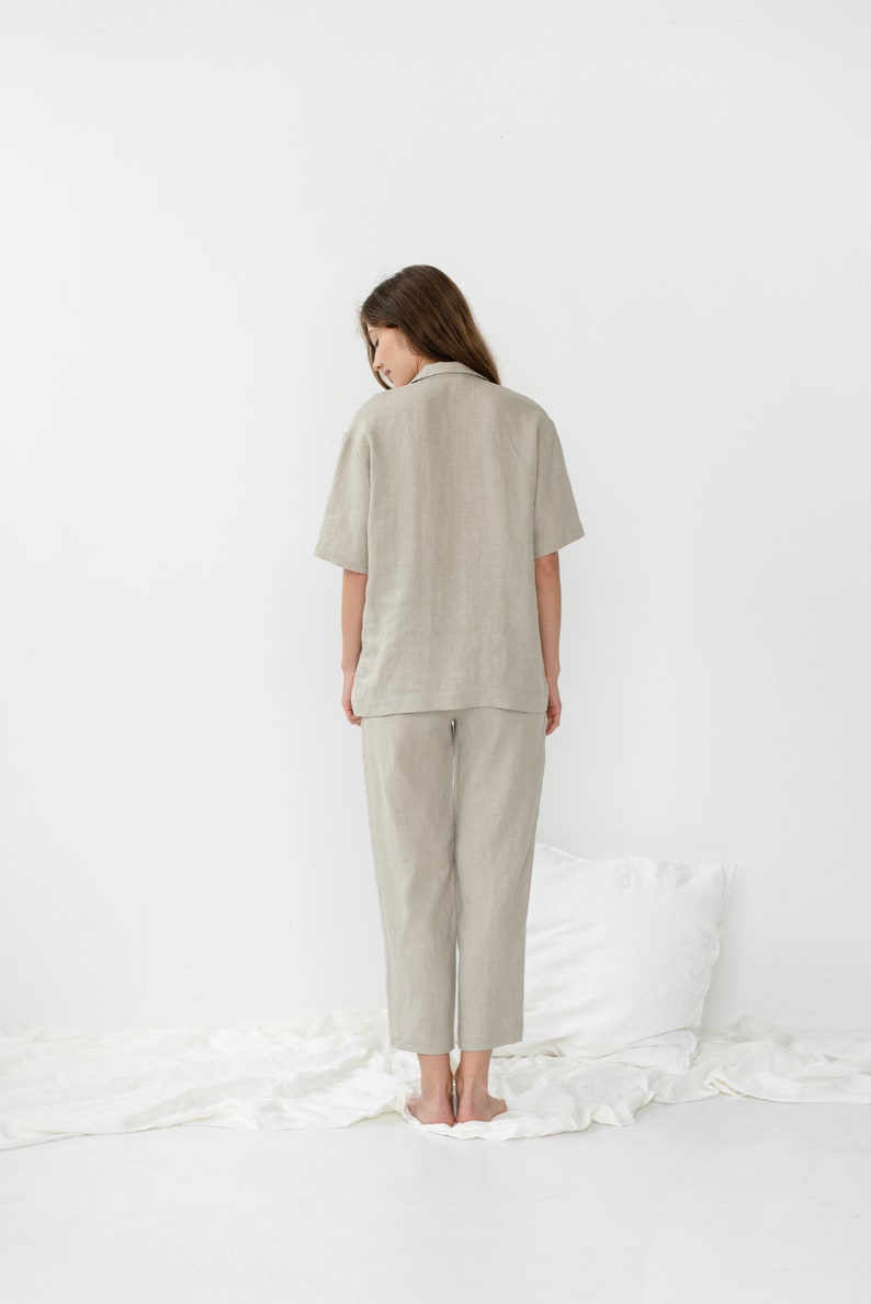 Pu&ograve; includere: Una persona indossa una camicia di lino beige chiaro e pantaloni abbinati. La camicia ha un colletto e maniche corte. I pantaloni sono corti e hanno una gamba dritta.