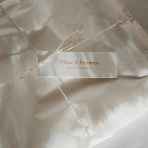 Pu&ograve; includere: Un pacco di carta bianca legato con uno spago e un'etichetta che recita "Pillow & Pajamas sleepwear, loungewear".