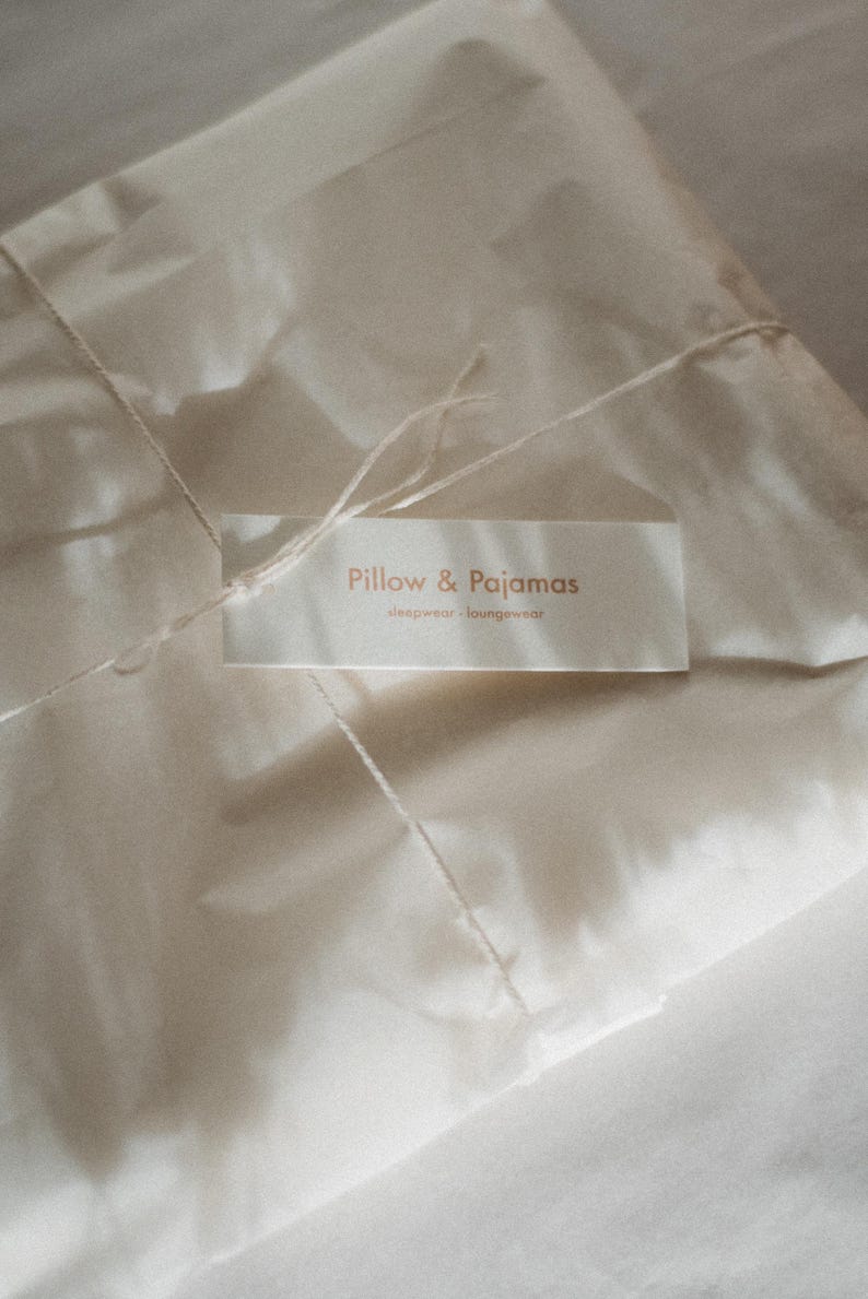 Pu&ograve; includere: Un pacco di carta bianca legato con uno spago e un'etichetta che recita "Pillow & Pajamas sleepwear, loungewear".