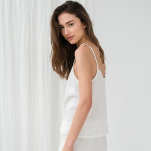 Peut inclure: Une femme portant un d&eacute;bardeur en lin blanc et un pantalon assorti. Le d&eacute;bardeur a un col rond et des bretelles fines. Le pantalon est ample et fluide.