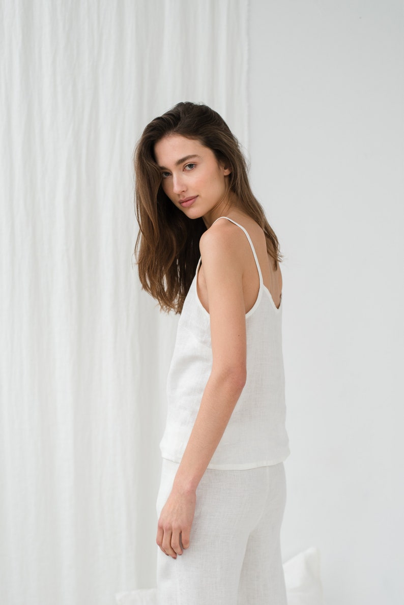 Peut inclure: Une femme portant un d&eacute;bardeur en lin blanc et un pantalon assorti. Le d&eacute;bardeur a un col rond et des bretelles fines. Le pantalon est ample et fluide.