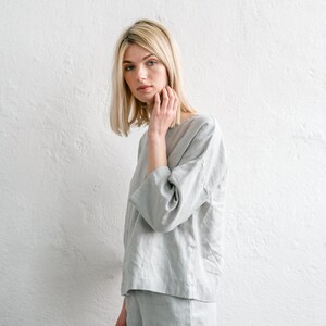 May include: A woman wearing a light grey linen top and matching shorts. The top has a relaxed fit and three-quarter sleeves. The shorts are a bit shorter and have a straight leg.