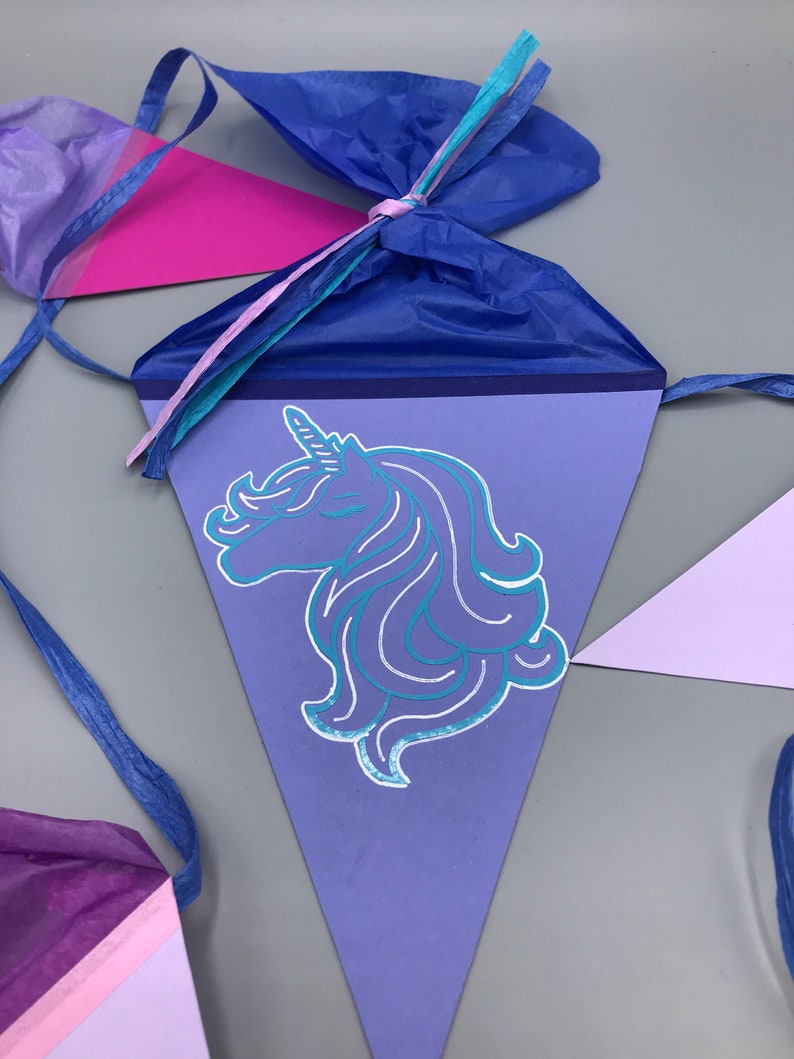Pu&ograve; includere: Striscione triangolare viola e blu con una silhouette di testa di unicorno al centro. L'unicorno ha un corno d'argento e una criniera blu. Lo striscione &egrave; legato con un nastro blu.