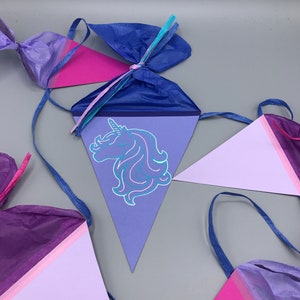 Pu&ograve; includere: Uno striscione per feste di unicorno viola, rosa e blu con decorazioni in carta velina. Lo striscione presenta una testa di unicorno con criniera e corno blu.