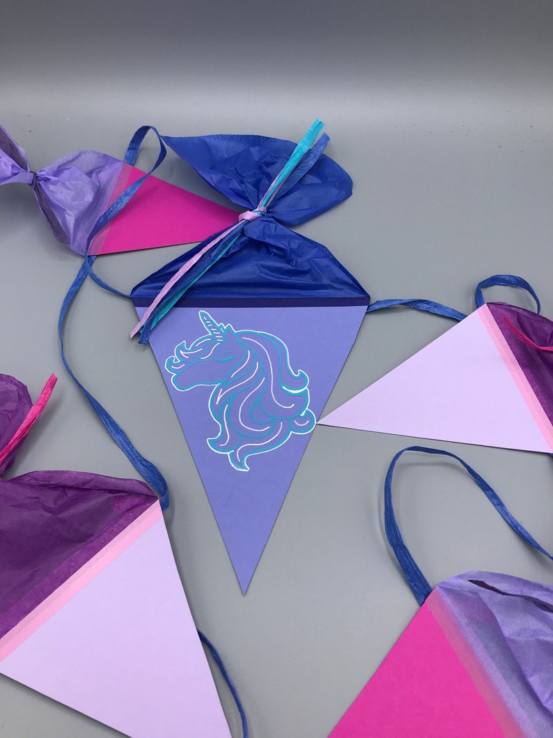 Pu&ograve; includere: Uno striscione per feste di unicorno viola, rosa e blu con decorazioni in carta velina. Lo striscione presenta una testa di unicorno con criniera e corno blu.