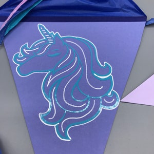 Pu&ograve; includere: Uno stendardo triangolare viola con una sagoma di unicorno turchese. L'unicorno ha un occhio chiuso e un corno bianco.