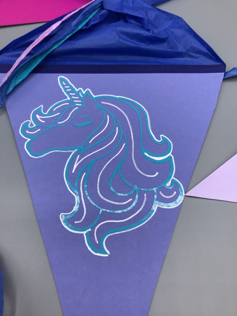 Pu&ograve; includere: Uno stendardo triangolare viola con una sagoma di unicorno turchese. L'unicorno ha un occhio chiuso e un corno bianco.