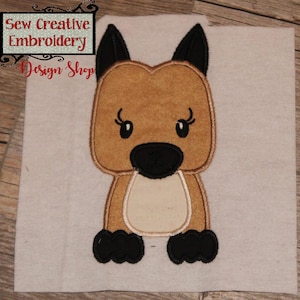 May include: Embroidered applique of a brown and black dog with big eyes and a white chest. The dog is sitting with its paws together. The applique is on a beige fabric background.