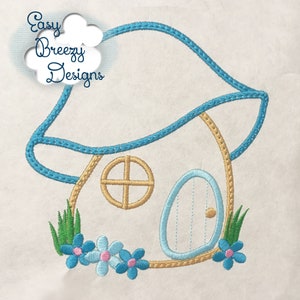 May include: An embroidered design of a whimsical fairy house with a blue roof and door, a round window, and a floral border. The text "Easy Breezy Designs" is in a cloud-shaped bubble.