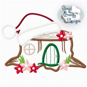 May include: Embroidered design of a small house made of a tree trunk with a green door, a window, and a red and white Santa hat on top. The house is surrounded by pink and red flowers.
