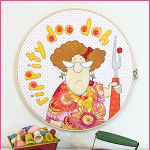Puede incluir: Una pieza de arte bordada de aro colorida con una mujer de dibujos animados sosteniendo un tenedor y el texto "doo dah" y "Li'l Pitiy". El arte del aro está rodeado de una colección de dedalitos coloridos y un carro de juguete rojo. También hay una plancha de juguete roja con un mango verde en la imagen.