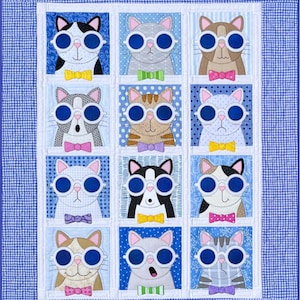 Könnte beinhalten: Eine blaue und weiße Patchwork-Decke mit einem sich wiederholenden Muster von Katzen, die Brillen und Fliegen tragen. Die Katzen sind in verschiedenen Farben und Mustern, darunter Schwarzweiß, Grau, Braun und dreifarbig.