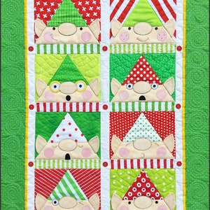 May include: A green, red, and white patchwork quilt with a design of eight elves. Each elf has a different hat and facial expression. The quilt is framed with a green border.
