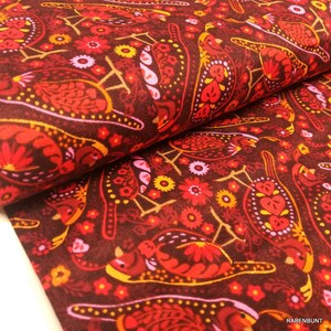 Könnte beinhalten: Nahaufnahme eines Stoffes mit einem sich wiederholenden Muster aus stilisierten Vögeln, Blumen und Paisley-Formen in Rot-, Orange-, Gelb- und Rosatönen auf einem dunkelbraunen Hintergrund. Der Stoff ist gefaltet und zeigt seine Textur.