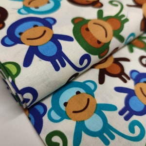 Könnte beinhalten: Weißer Stoff mit einem sich wiederholenden Muster aus blauen, grünen und braunen Affen. Die Affen haben lächelnde Gesichter und sind in verschiedenen Posen.