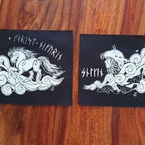 Pode incluir: Dois patches de tecido preto com ilustrações brancas. Um apresenta um cavalo com texto acima, o outro retrata uma figura com um capacete e texto. Ambos os desenhos são rodeados por padrões em redemoinho semelhantes a nuvens.