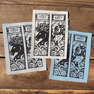 May include: Three fabric patches featuring black and white illustrations of mythical creatures. The patches are rectangular and have a white background with black outlines. The text "Hvítr" and "Sámi" is printed on the patches.