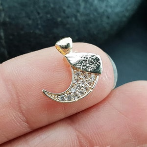 Peut inclure: Breloque en forme de croissant de lune doré avec des strass transparents. Le breloque a une surface texturée et une boucle pour l'attacher à des bijoux.