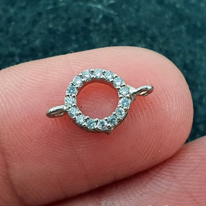 May include: A silver-toned round connector with a circle of clear rhinestones. The connector has two loops on either side for attaching jewelry.