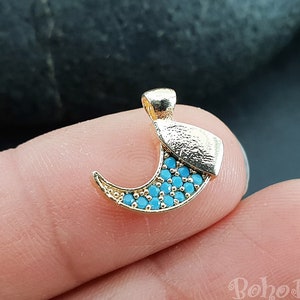 Peut inclure: Charme de lune croissante en or avec des pierres turquoise bleues. Le charme est sur un doigt.