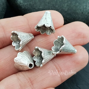 May include: Five silver metal cone-shaped bead caps with scalloped edges. The caps are approximately 1 inch in diameter.