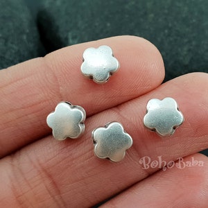 May include: Four silver flower-shaped beads, each with five petals, are shown on a hand. The beads are approximately 1.2 cm in diameter.