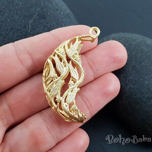 May include: Gold-toned metal pendant with a crescent moon shape and a detailed floral design. The pendant has a loop at the top for attaching to a chain or cord.