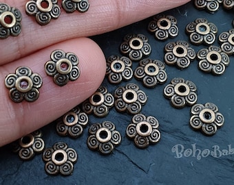 May include: A close-up of a pile of antique gold-toned metal bead caps with a swirl design. The caps have a small hole in the center for stringing.