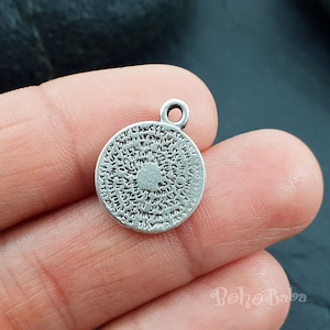 Puede incluir: Encanto de plata con un diseño circular que presenta patrones intrincados y un pequeño corazón en el centro. El encanto tiene un bucle en la parte superior para sujetarlo a un collar o pulsera.
