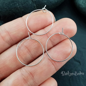 May include: Three silver hoop earrings of different sizes. The earrings are shown on a hand against a dark background.