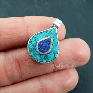 May include: A silver pendant in the shape of a teardrop with a blue and turquoise stone inlay. The stone is set in a silver frame and has a silver loop at the top for attaching to a chain.
