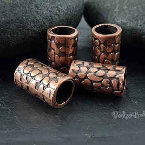 May include: Four copper-colored metal beads with a textured, patterned surface. The beads are cylindrical and have a slightly rounded edge.